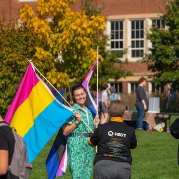 student with two PRIDE flags at outdoor event on campus mall
