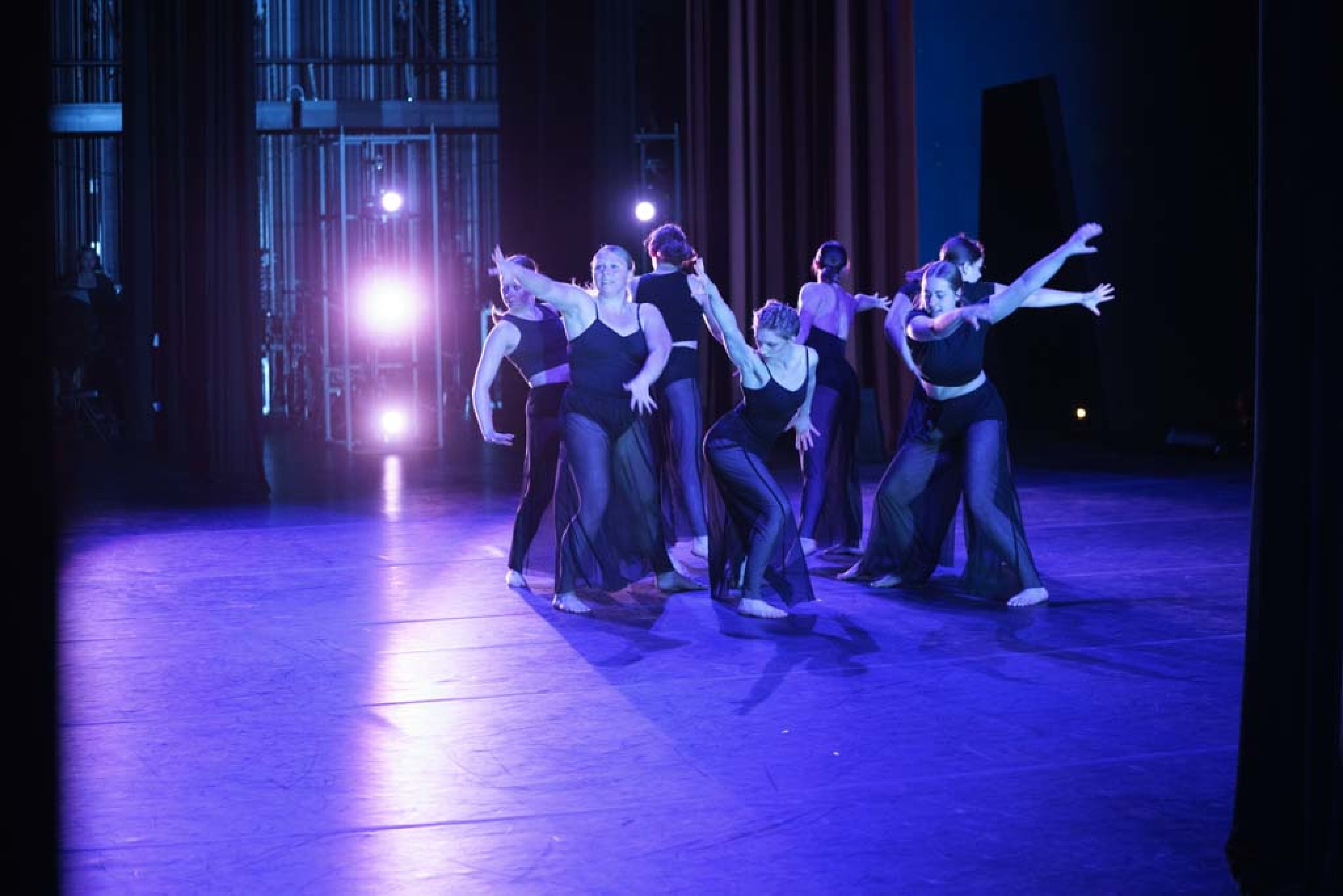 dancers in black costumes on stage with blue light