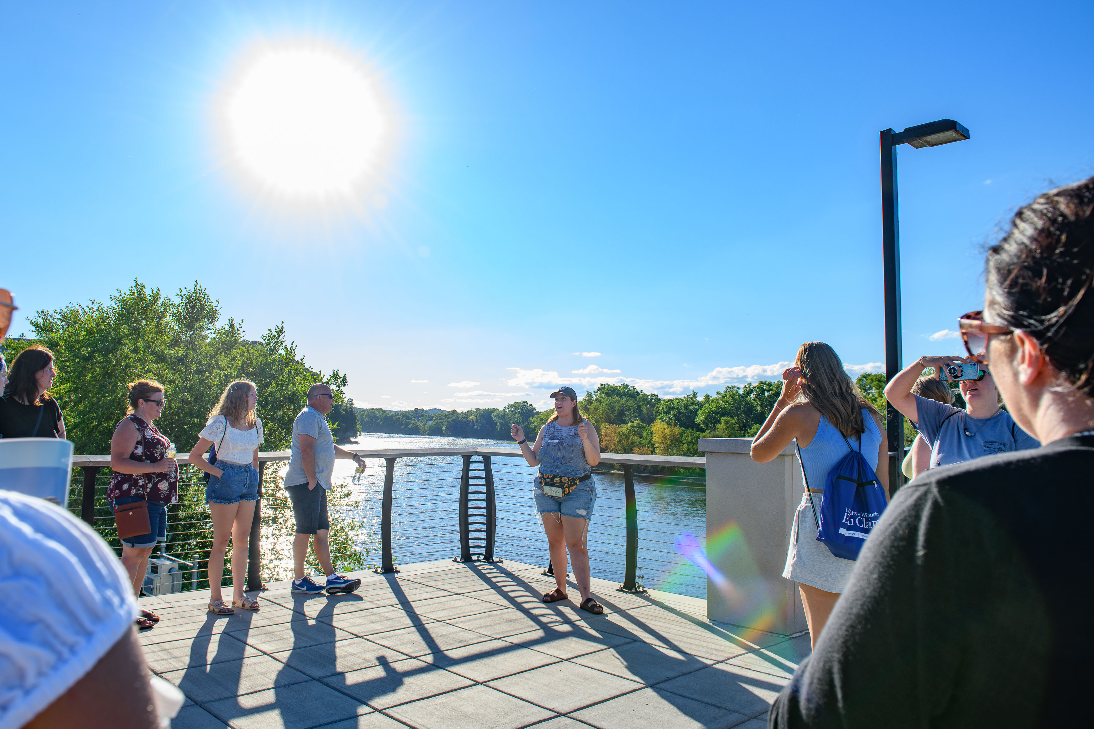 Campus visitors listen to a tour guide near the river during a sunny Sunset campus visit.