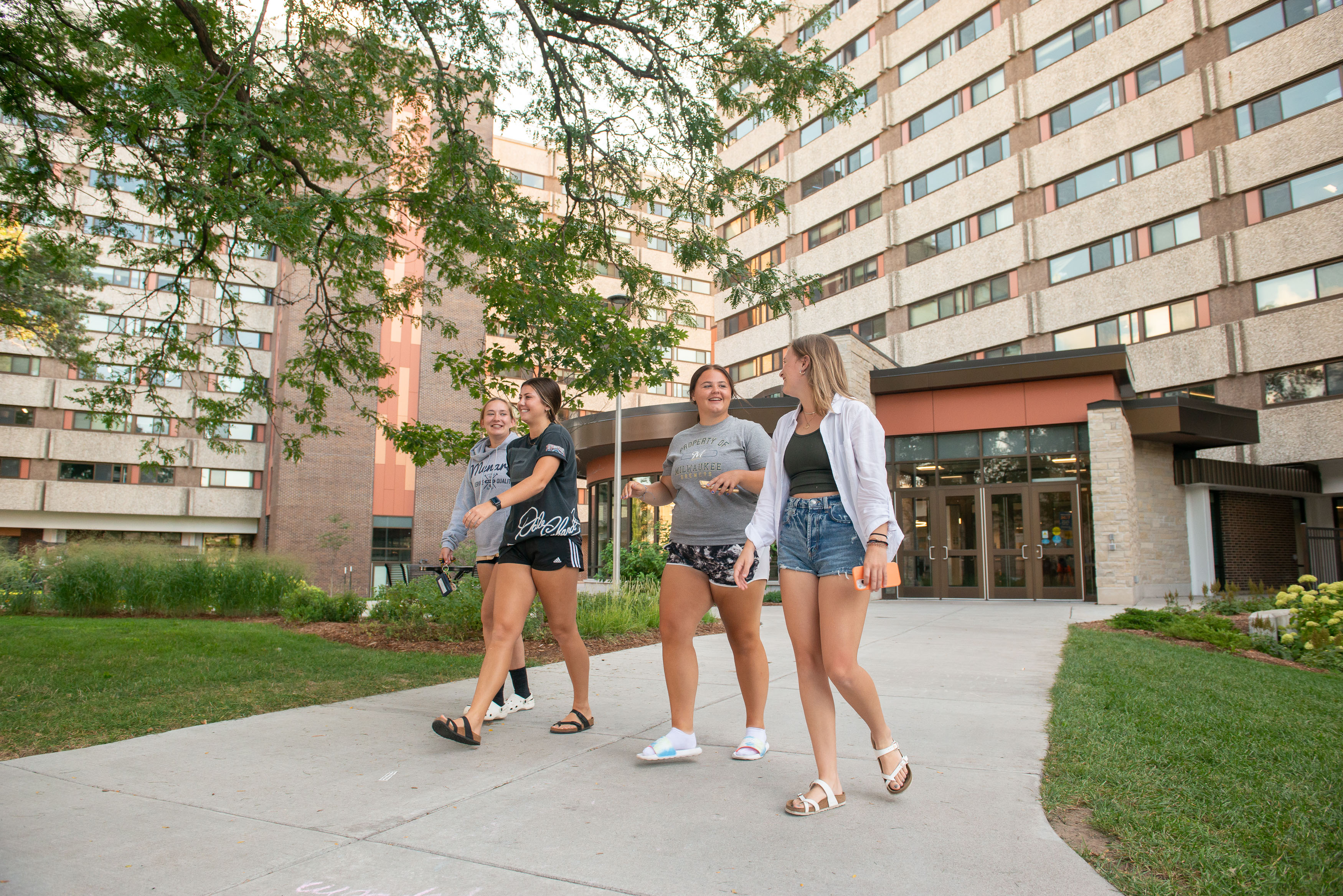 Students laughing and walking on the sidewalk on upper campus near Karlgaard Towers entrance.