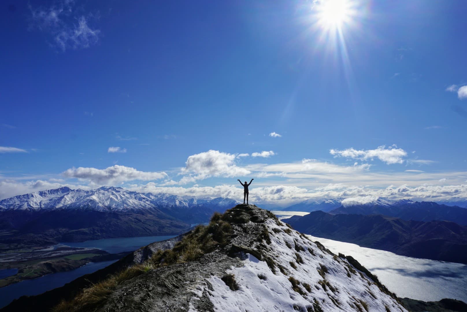 A student on a study abroad program in New Zealand standing at the peak of mountain with a large landscape mountain background