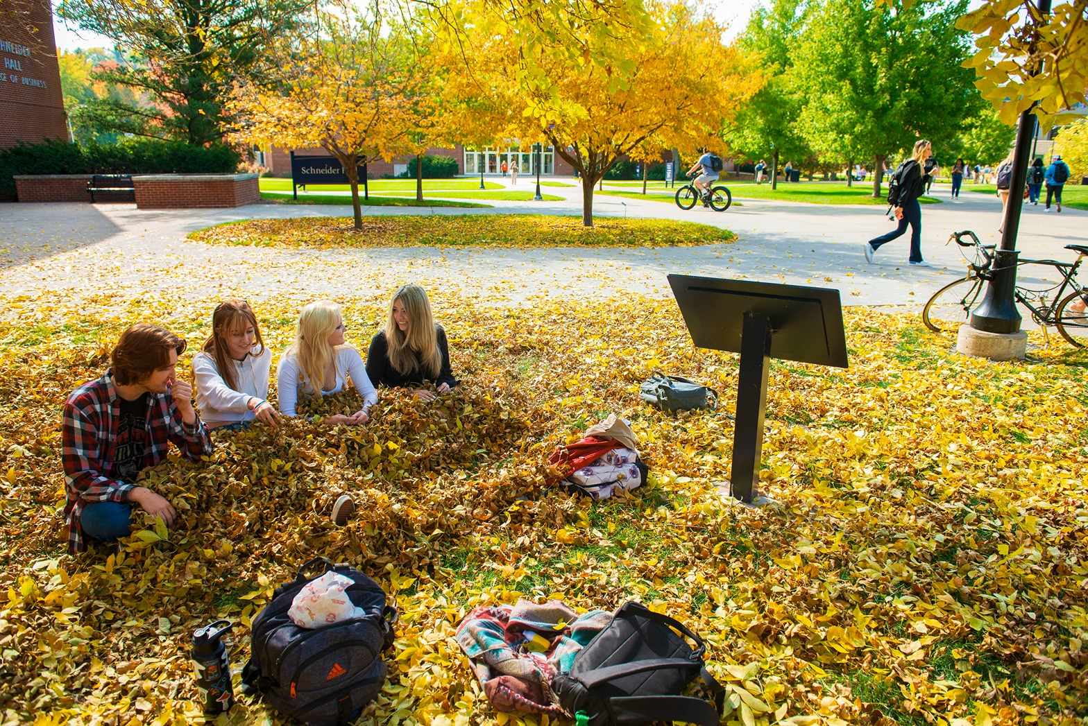 students in a leaf pile outside college of business 