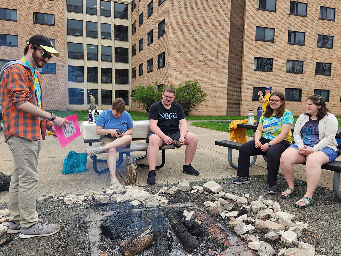 a group of students sit around a grill outdoors