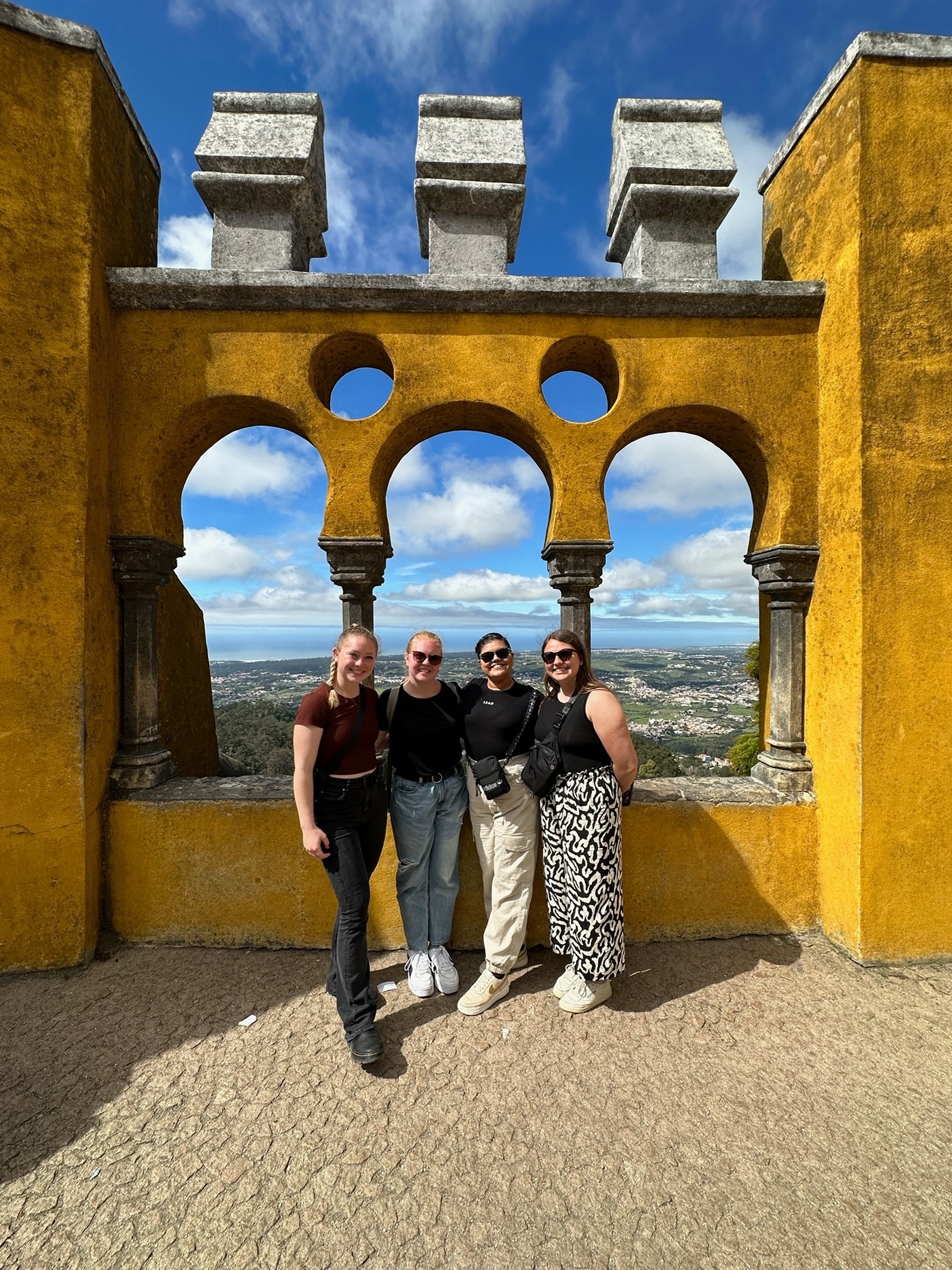 four students standing in a yellow stucco international building 