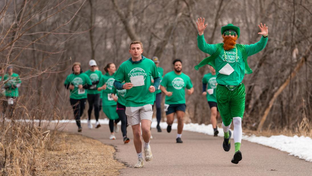 Man dressed as leprechaun running on river path