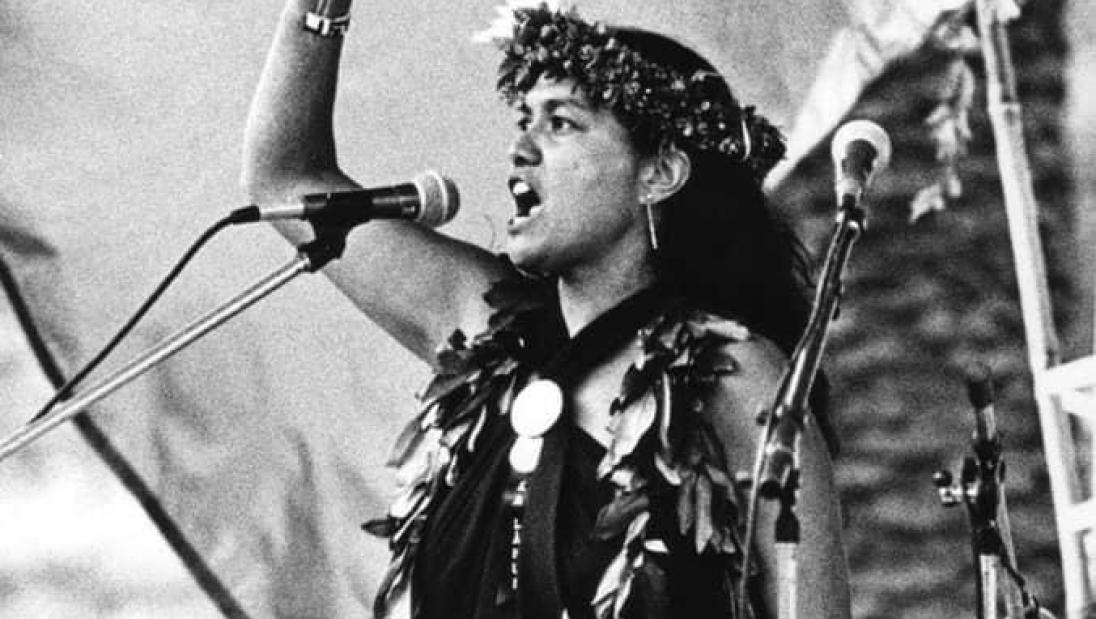A woman stands in profile, with her fist raised in the air.