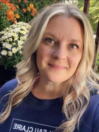 Professor Meinen smiling, wearing a UWEC shirt, with flowers behind her