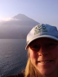 A person smiling in front of water and a mountain