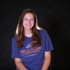 Kathryn smiles for camera in front of black backdrop.
