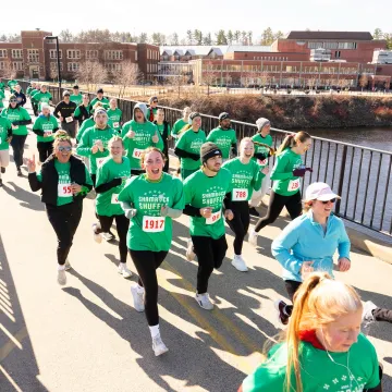 runners in green shirts crossing campus footbridge for a race 