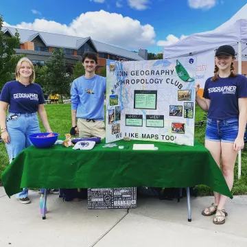 students in Geography club t-shirts at a table event outdoors 