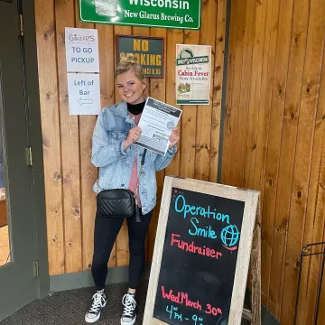 a student standing near a sign for an Operation Smile Club event 