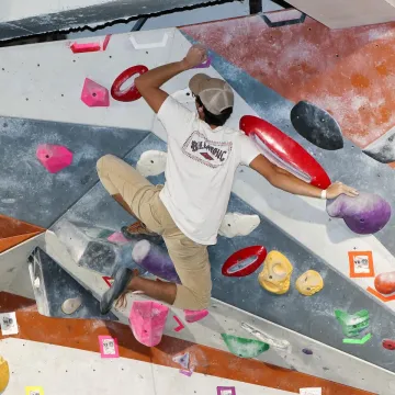 student on the bouldering wall, with club t-shirt on 