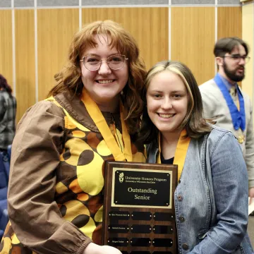 two graduating seniors smile with a plaque