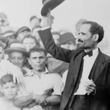 Black and white photograph of a man raising his hat to a crowd of onlookers.