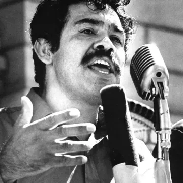 Black and white picture of a man speaking into a microphone at a lecturn.