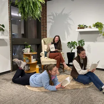 Students sitting among plants readying a book in foster gallery