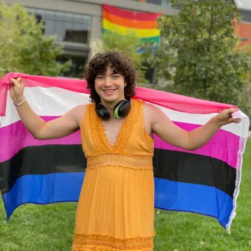 A person holding a pride flag smiles for the camera. 