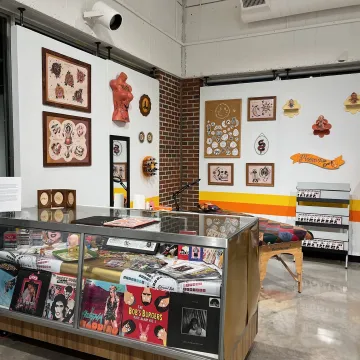 Detail installation of Carly Bower's project that brought a tattoo parlor setup inside the foster gallery. Shown is a display case, posters, and tattoo table