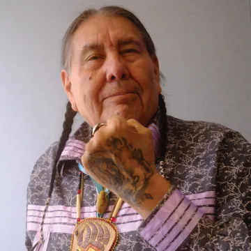 A man faces the camera with a tattooed fist in front of his mouth.