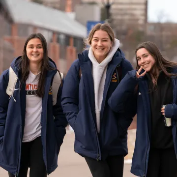 three students in winter coats posing for a smiling photo outside on first day of classes in Jan. 