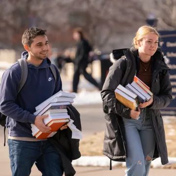 Frist day of spring classes, students walking outside with book stacks 