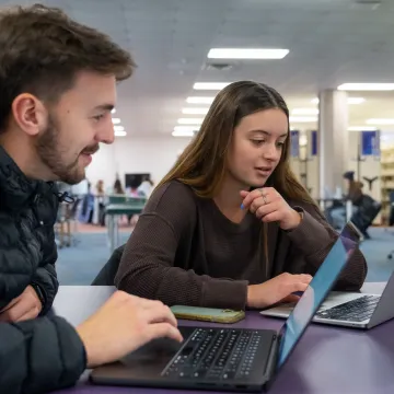 two students at a table in McIntyre Library looking at laptops 