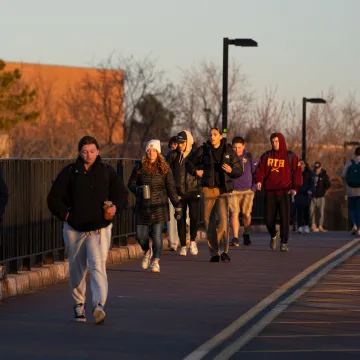 Crowd of students crossing the footbridge, winter jackets, sunny day 