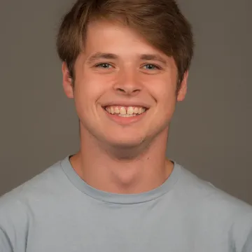 White male presenting person with short brown hair and wearing a blue T-shirt. He is smiling.