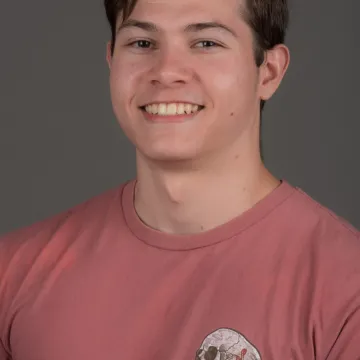 a white male presenting person with brown hair. He is wearing a red shirt and is smiling.