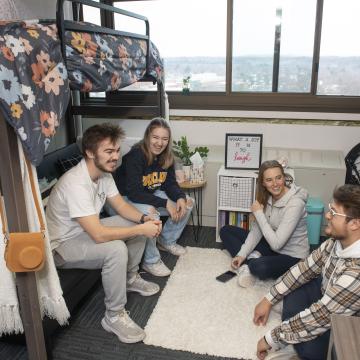 four students in a residence hall room chatting