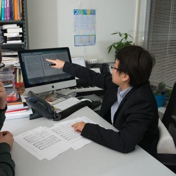 Two people look at a computer screen showing sheet music