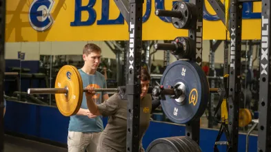 student spotting a client doing a squat in the weight room
