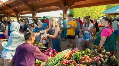 Woman purchasing a bag of strawberries from a stand selling multiple fruits and vegetables