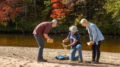 A professor kneels down and pours sand into his hand while two students smile and observe