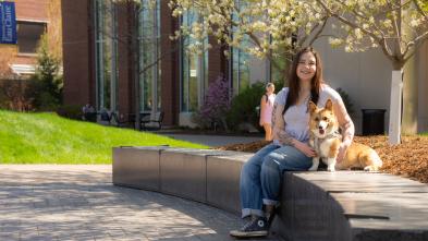 student and service dog seated on campus mall area on a sunny spring day