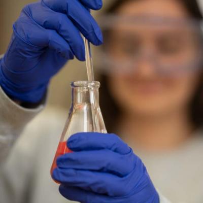 BioMed lab student holding a beaker, blue gloves 