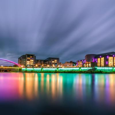 Pablo Center as viewed from across the river at night with the bridge lit up.