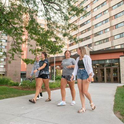 Students laughing and walking on the sidewalk on upper campus near Karlgaard Towers entrance.