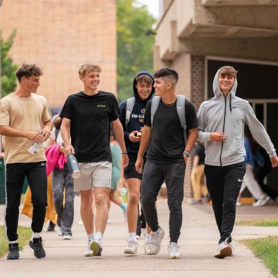 Students laughing and walking on the sidewalk on upper campus.