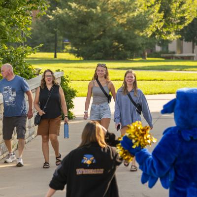 students and family crossing campus mall bridge facing Blu with spirit gear 