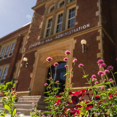 Pink flowers in front of Schofield Hall on a sunny day.