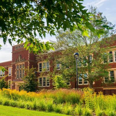 Brick campus building on a sunny day behind trees with green leaves