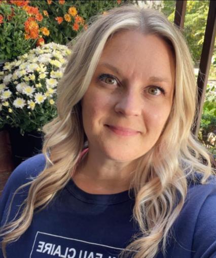 Professor Meinen smiling, wearing a UWEC shirt, with flowers behind her