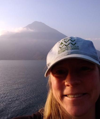 A person smiling in front of water and a mountain