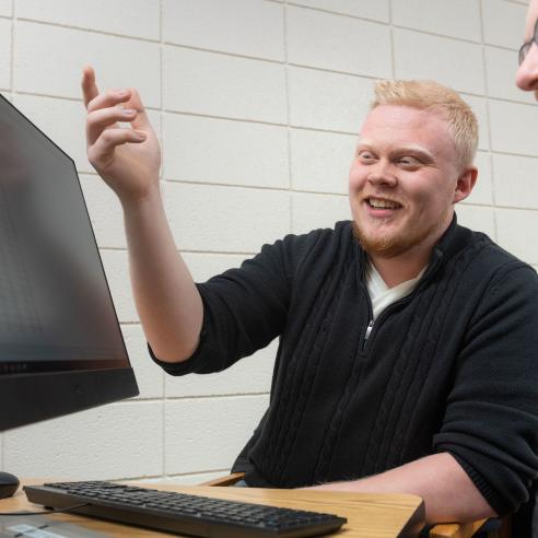 A man and a woman are interacting joyfully in front of a computer in an office setting