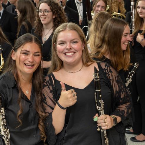 Joyful music students holding clarinets and a saxophone surrounded by band peers