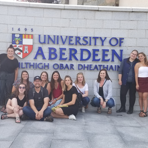 A group photo of students on an immersion trip in Scotland, posing in front of a University of Aberdeen