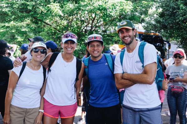 three adults posing for a group photo outdoors, man on right wearing a Packer cap