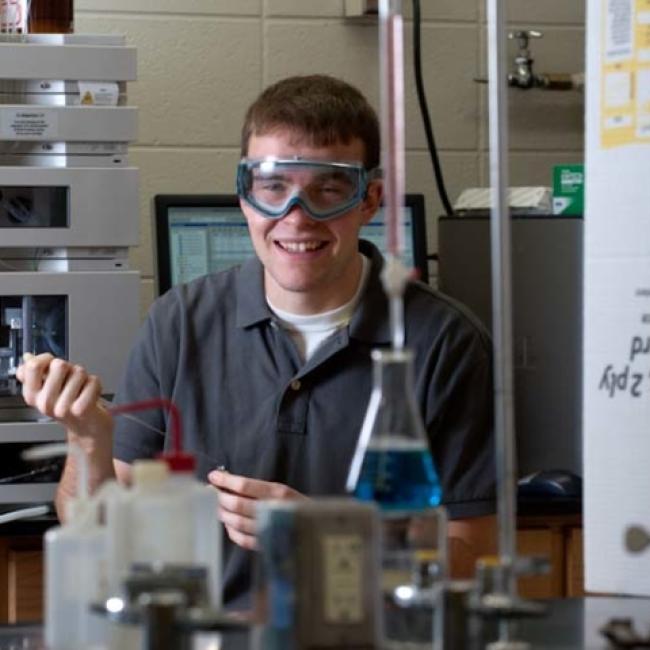 Student using chemistry equipment in a lab wearing goggles